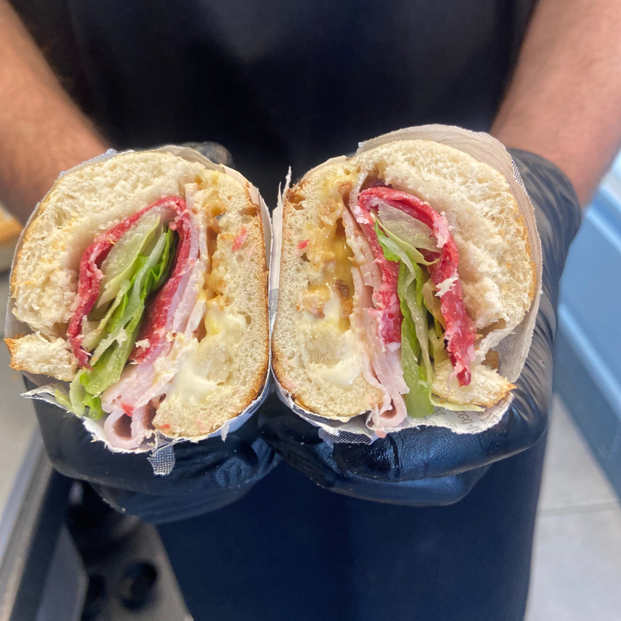 Sandwich à la charcuterie française coupé en deux : dinde, salami et laitue, tenu devant le tablier de la maison