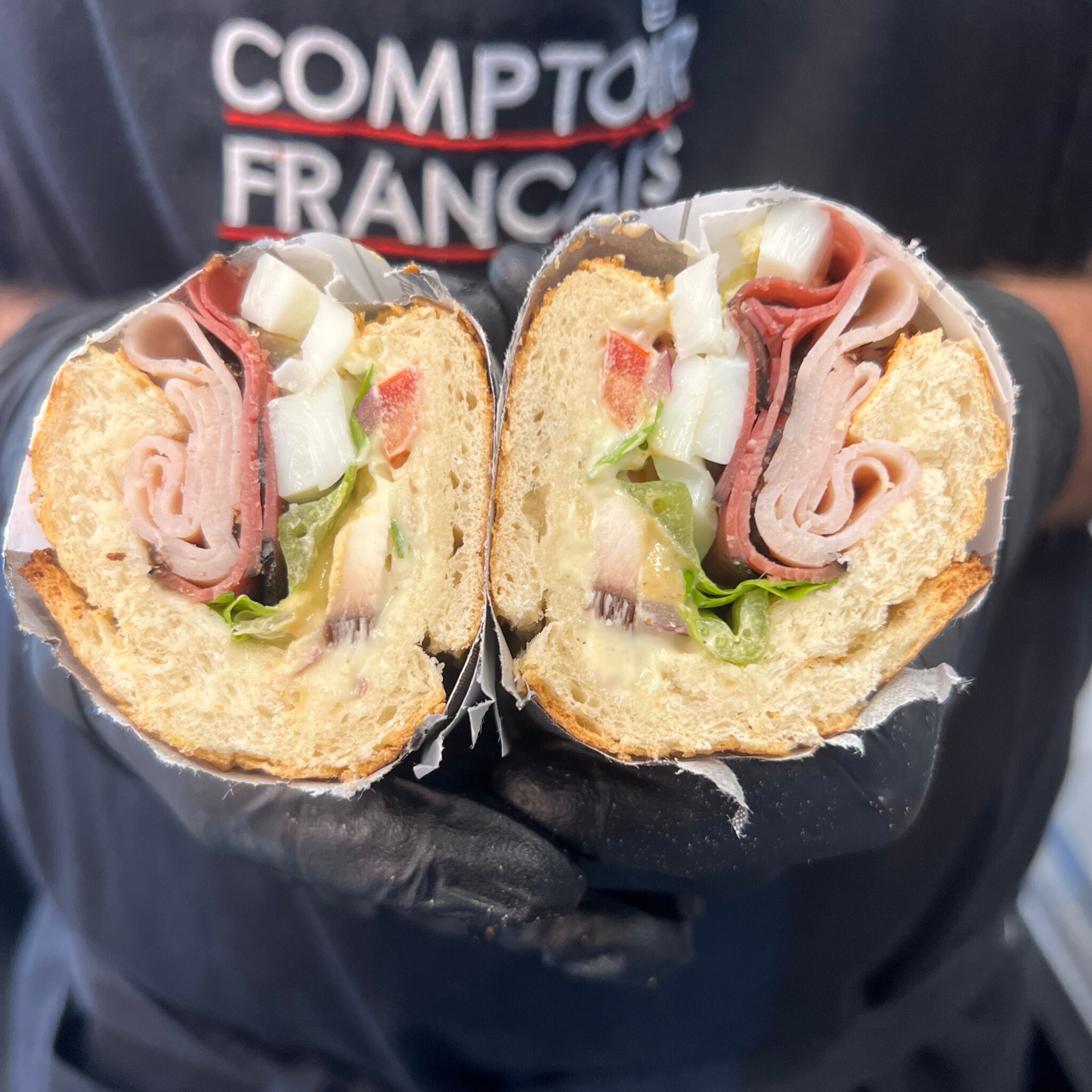Sandwich à la charcuterie garni de dinde, pastrami, oignon et laitue, coupé en deux