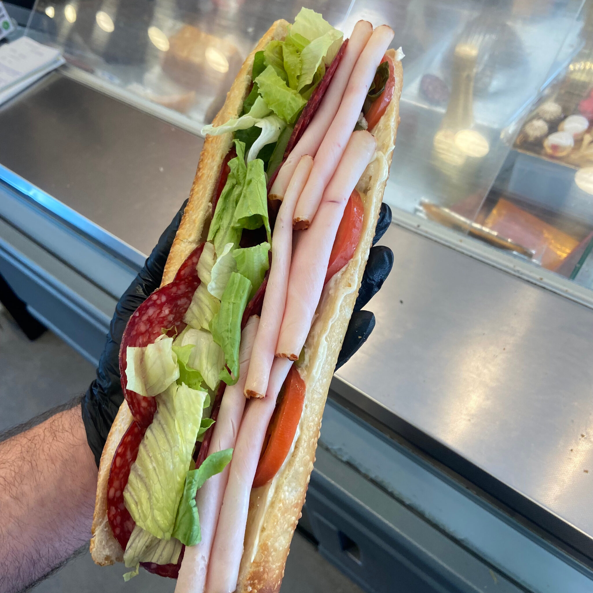 Baguette française garnie de charcuterie, laitue et tomate, préparée au comptoir