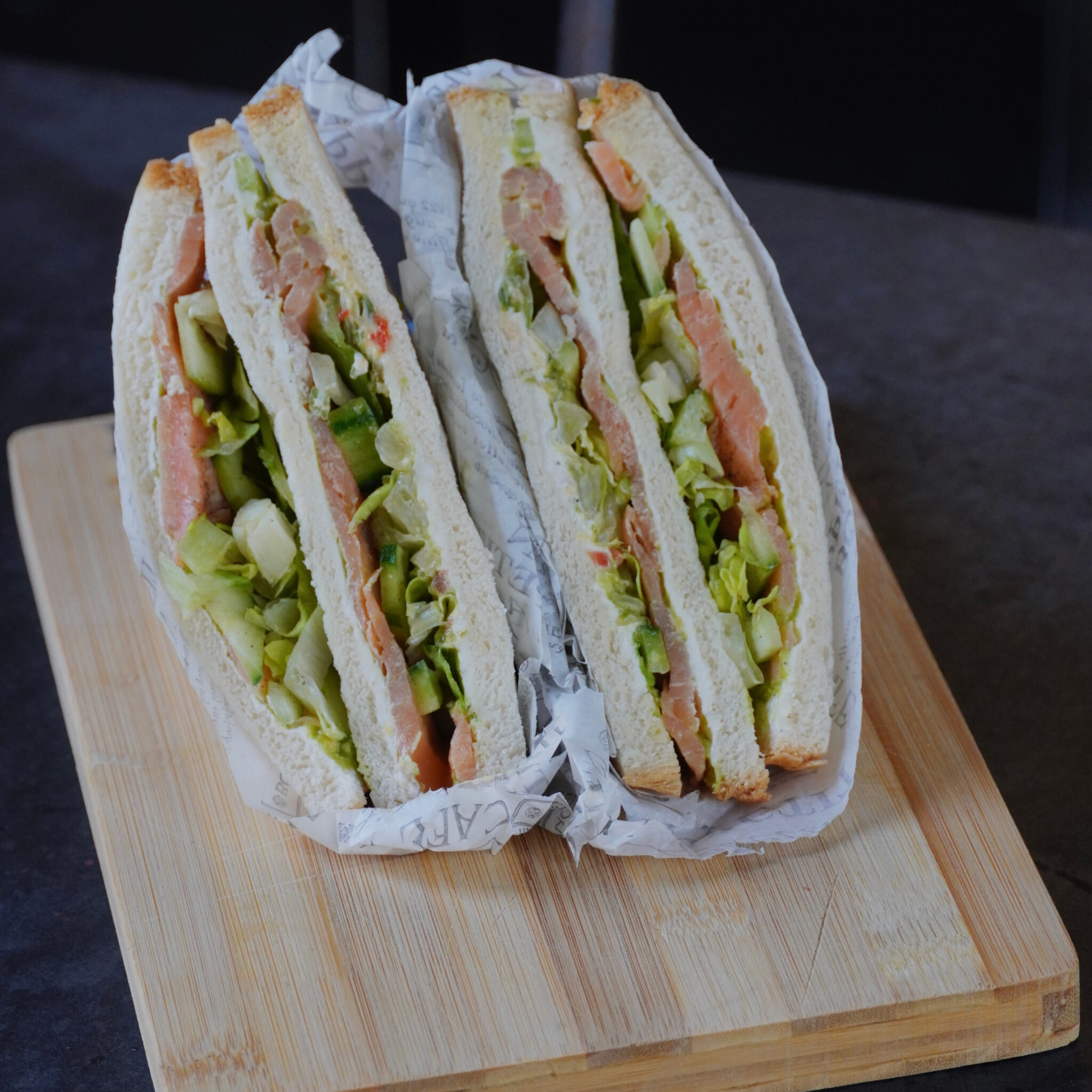 Club sandwich au saumon fumé et crudités, coupé en deux et servi dans son papier